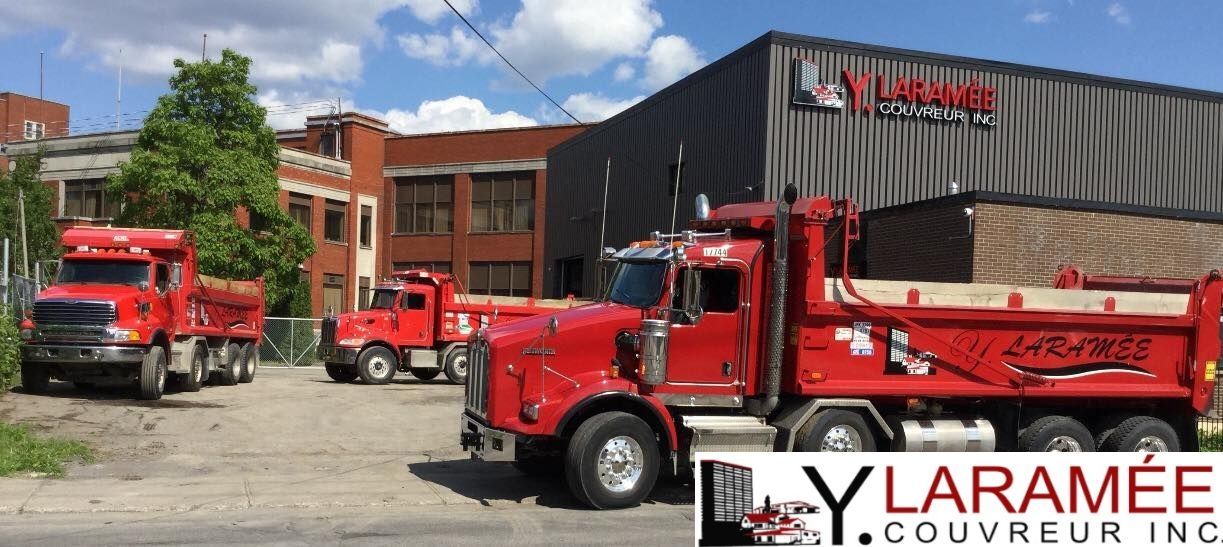 Trois camions à benne rouges sont garés devant un bâtiment.