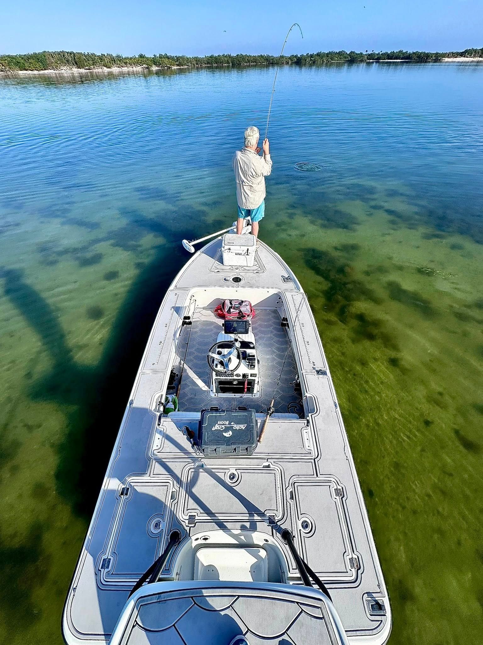 Person fishing from a boat in shallow, clear water; rod raised.