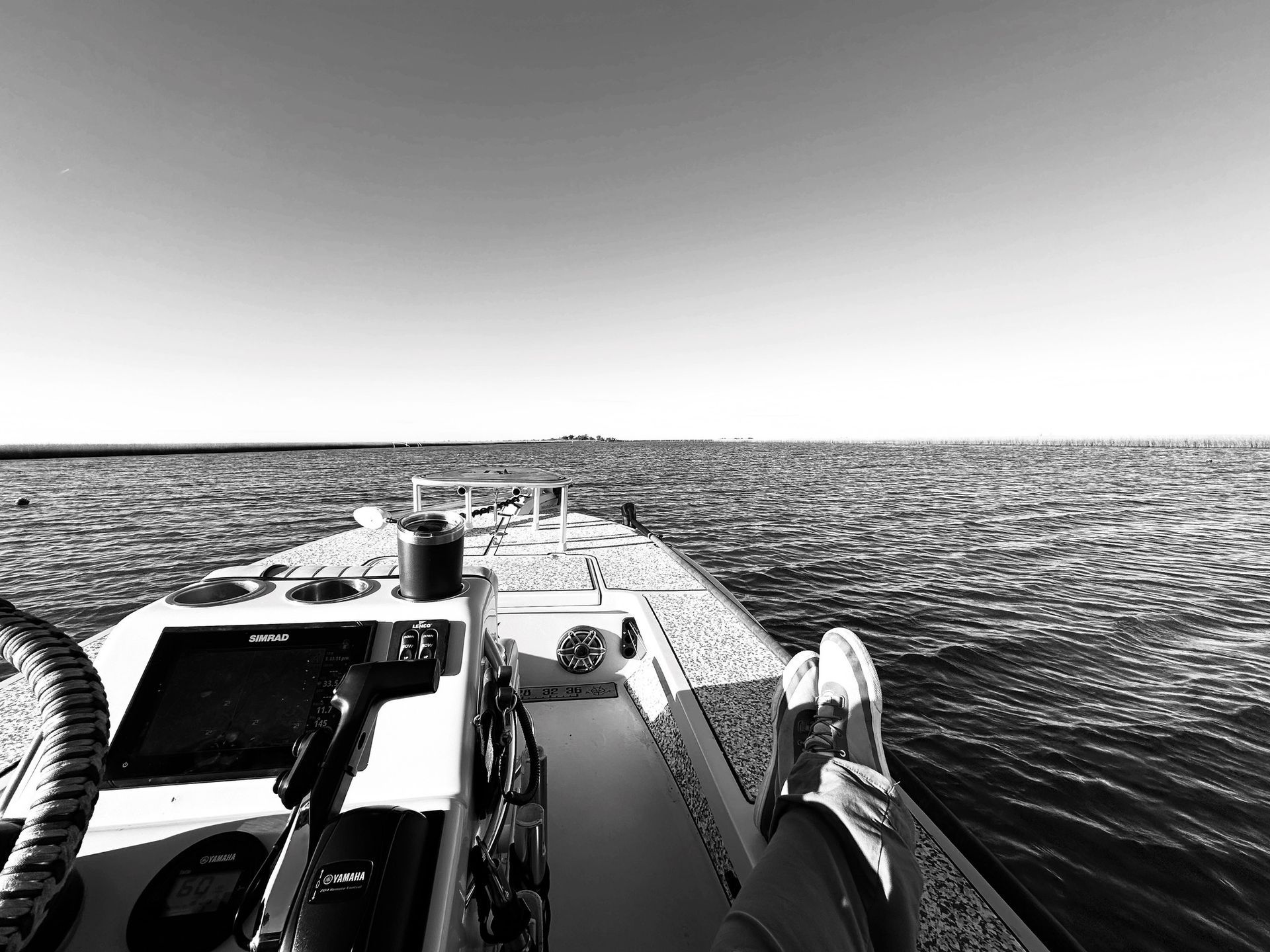 Black and white view from a boat's deck, looking out over the water towards the horizon on a sunny day.