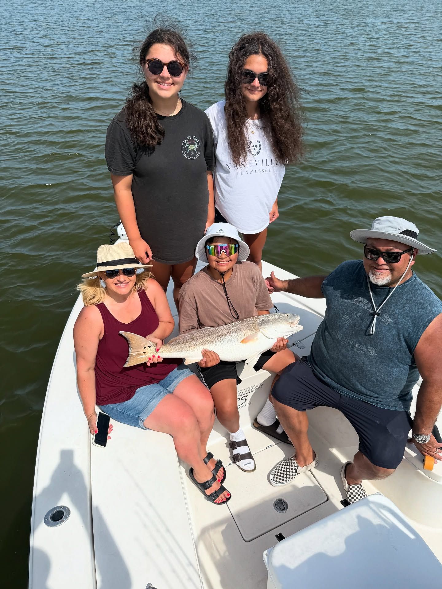 Group of people on a boat fishing. Holding up a large red fish in sunlight, with water in the background.