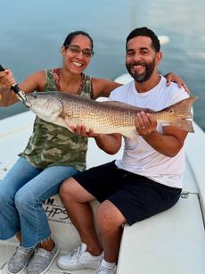 Couple on a boat holding a large fish, smiling. Sunny day, water background.