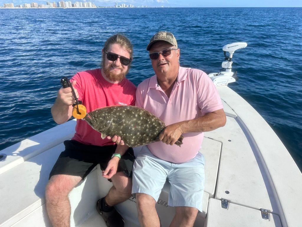 Two men on a boat show off a large, speckled fish. Ocean and buildings in the background.