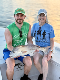 Man and woman on a boat, holding a fish. The man smiles. Sunset in the background.