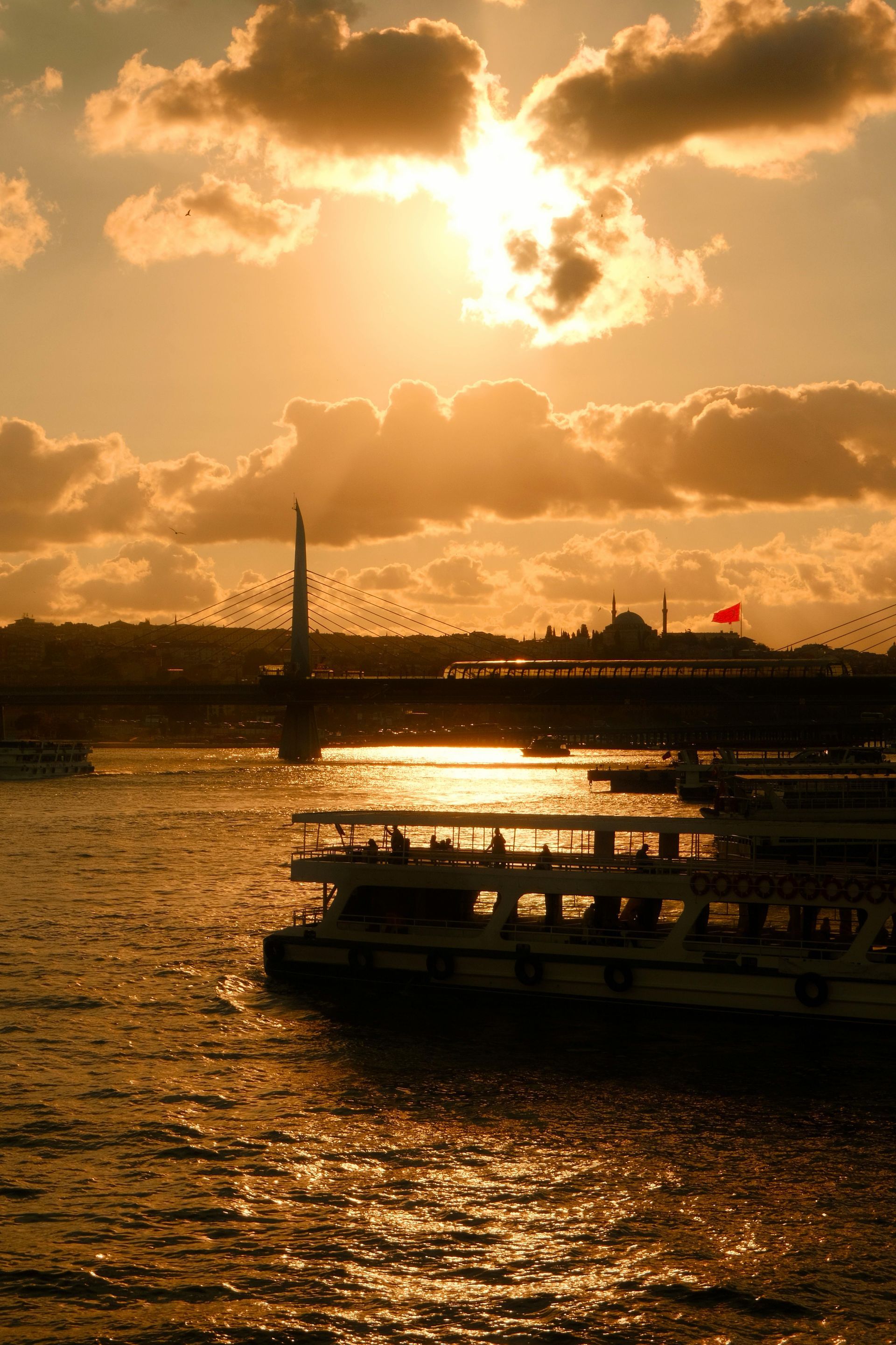 Sunset over Istanbul, silhouetted bridge and boats on the water, golden light.