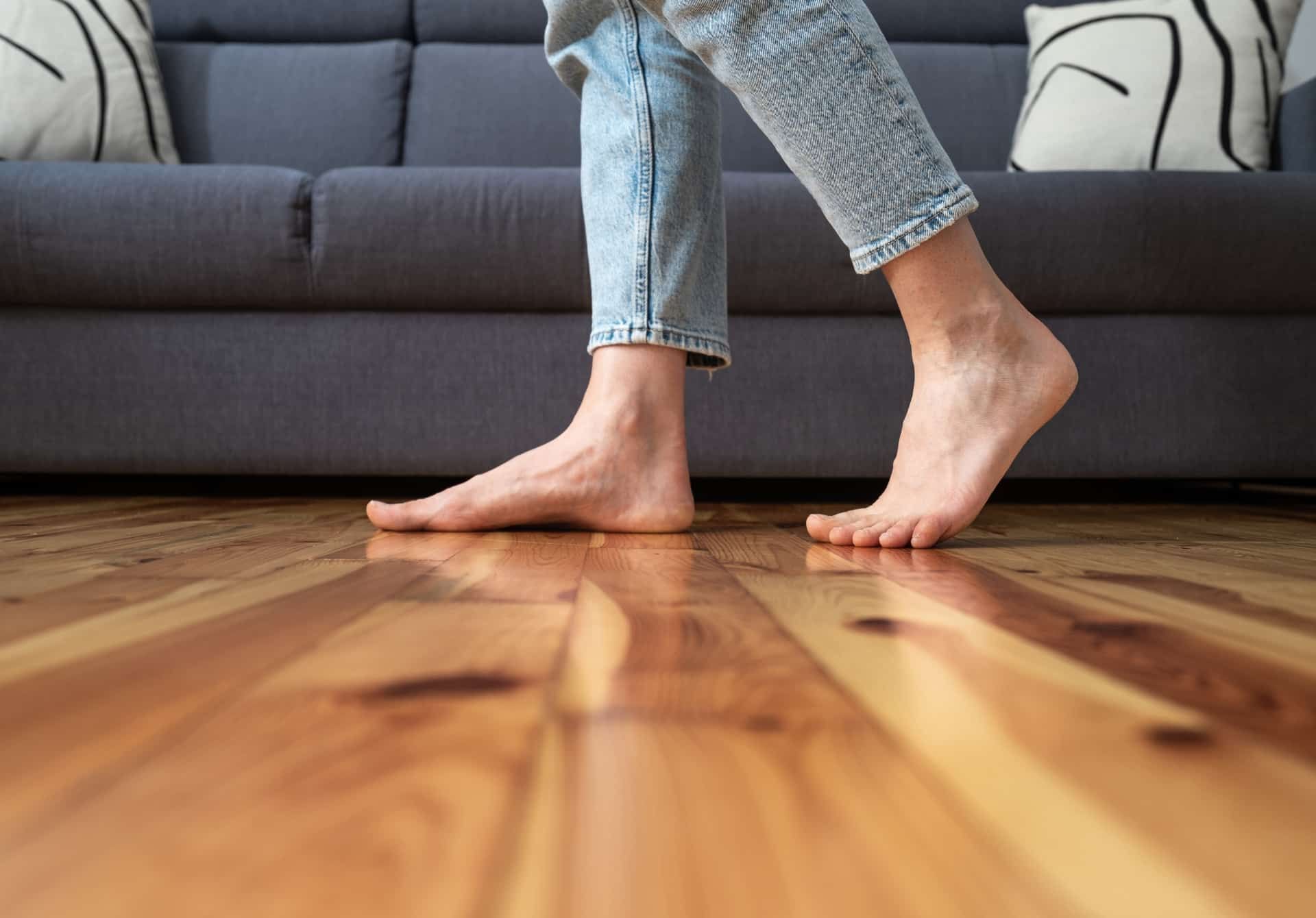 A person is walking barefoot on a wooden floor in a living room.