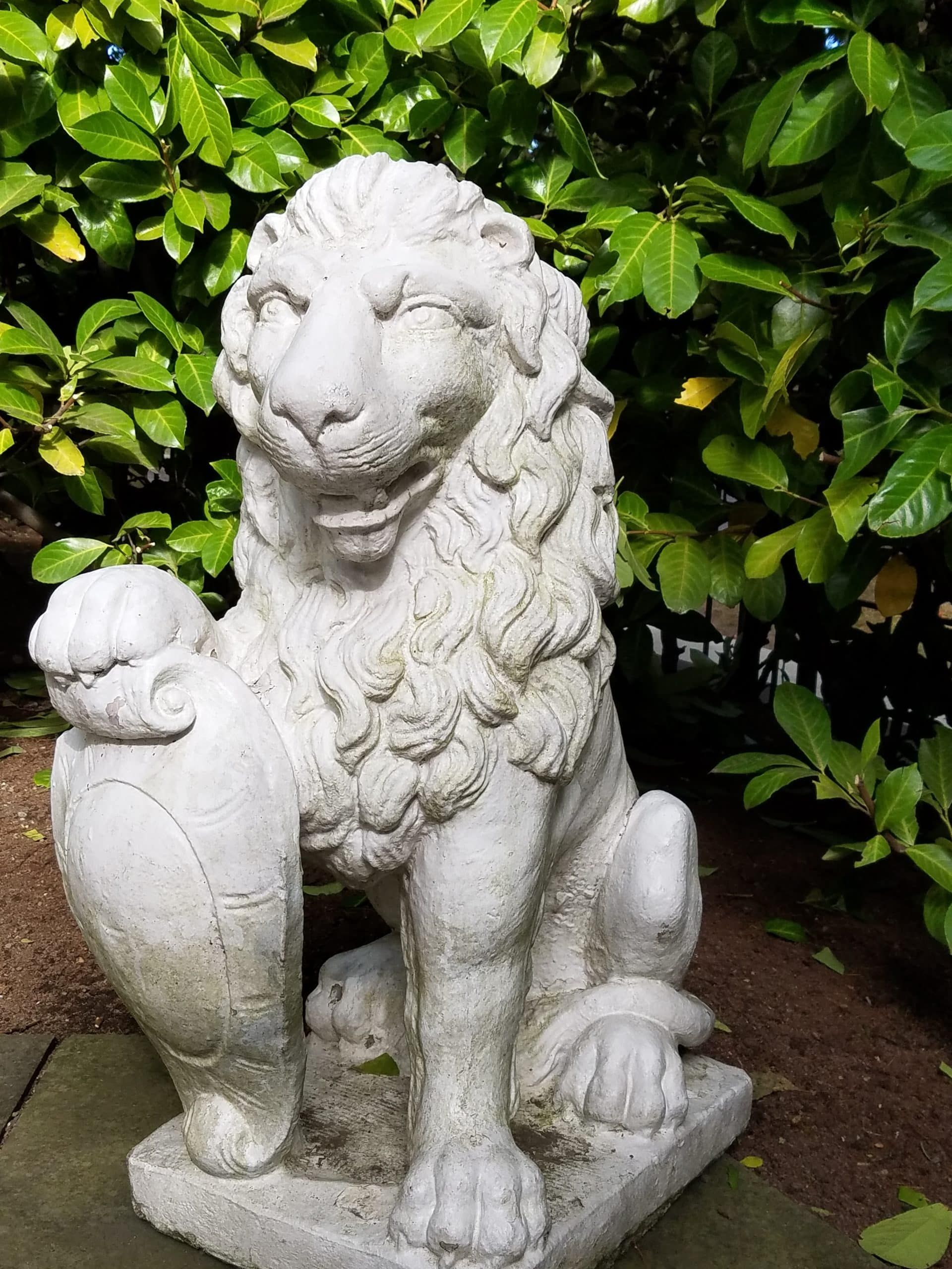 A statue of a lion is sitting in front of a bush.