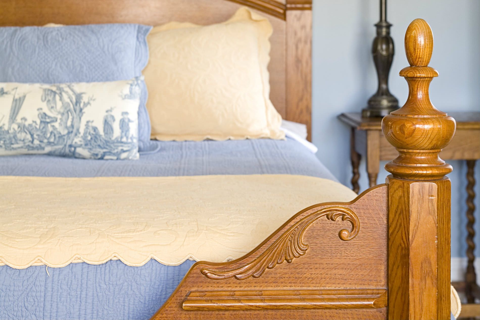A wooden bed with a blue blanket and white pillows