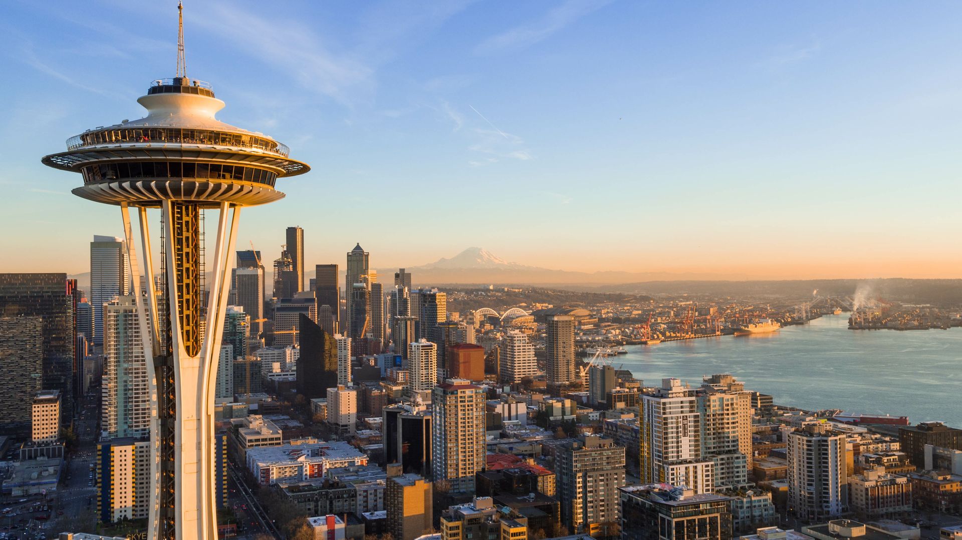 Space Needle and Seattle skyline at sunset, with a mountain in the background.