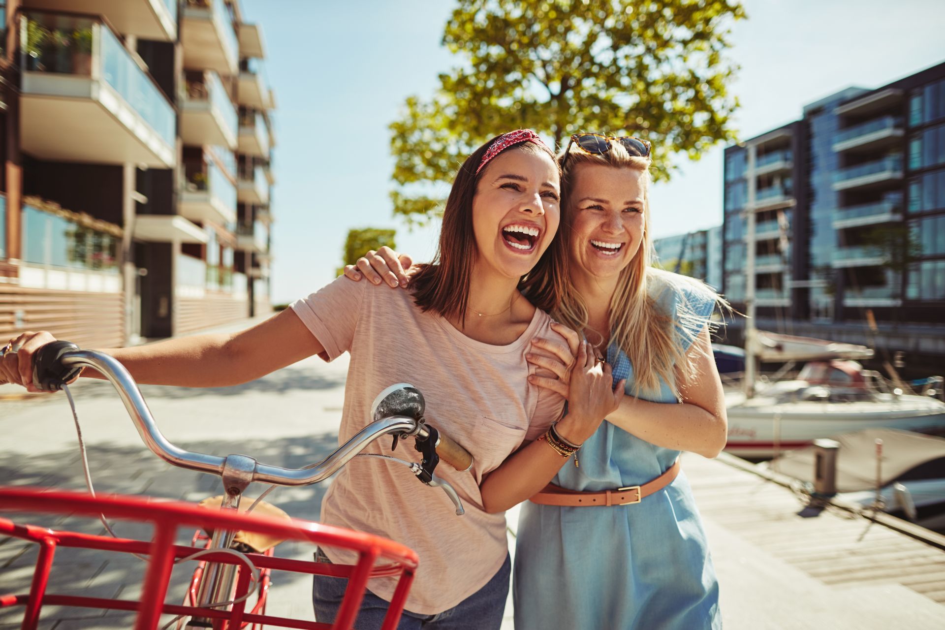 Two women are laughing while standing next to a bicycle.