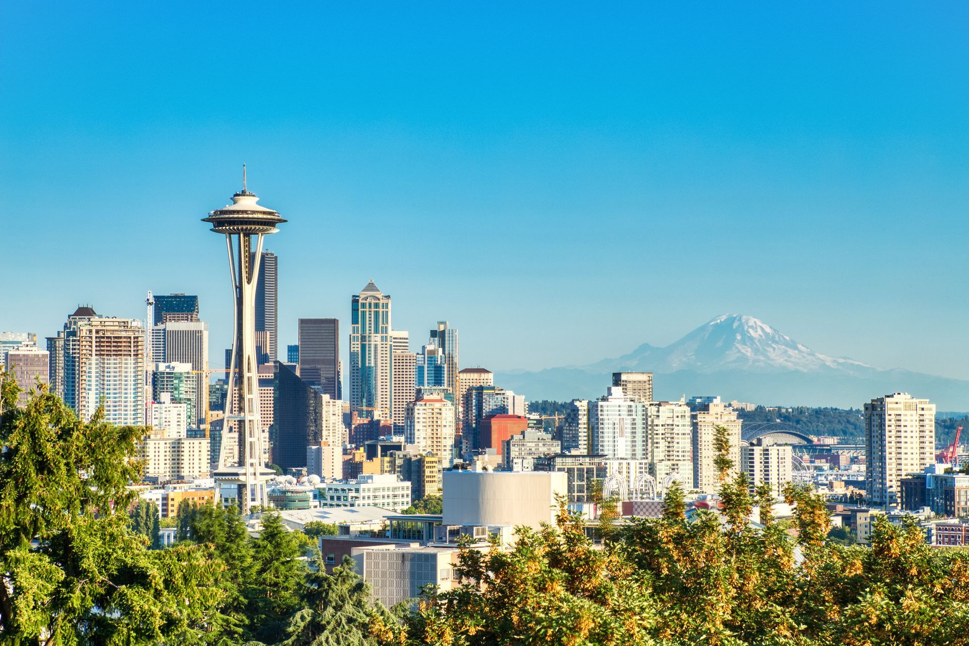 Seattle skyline with Space Needle, buildings, blue sky, and Mount Rainier in the background.