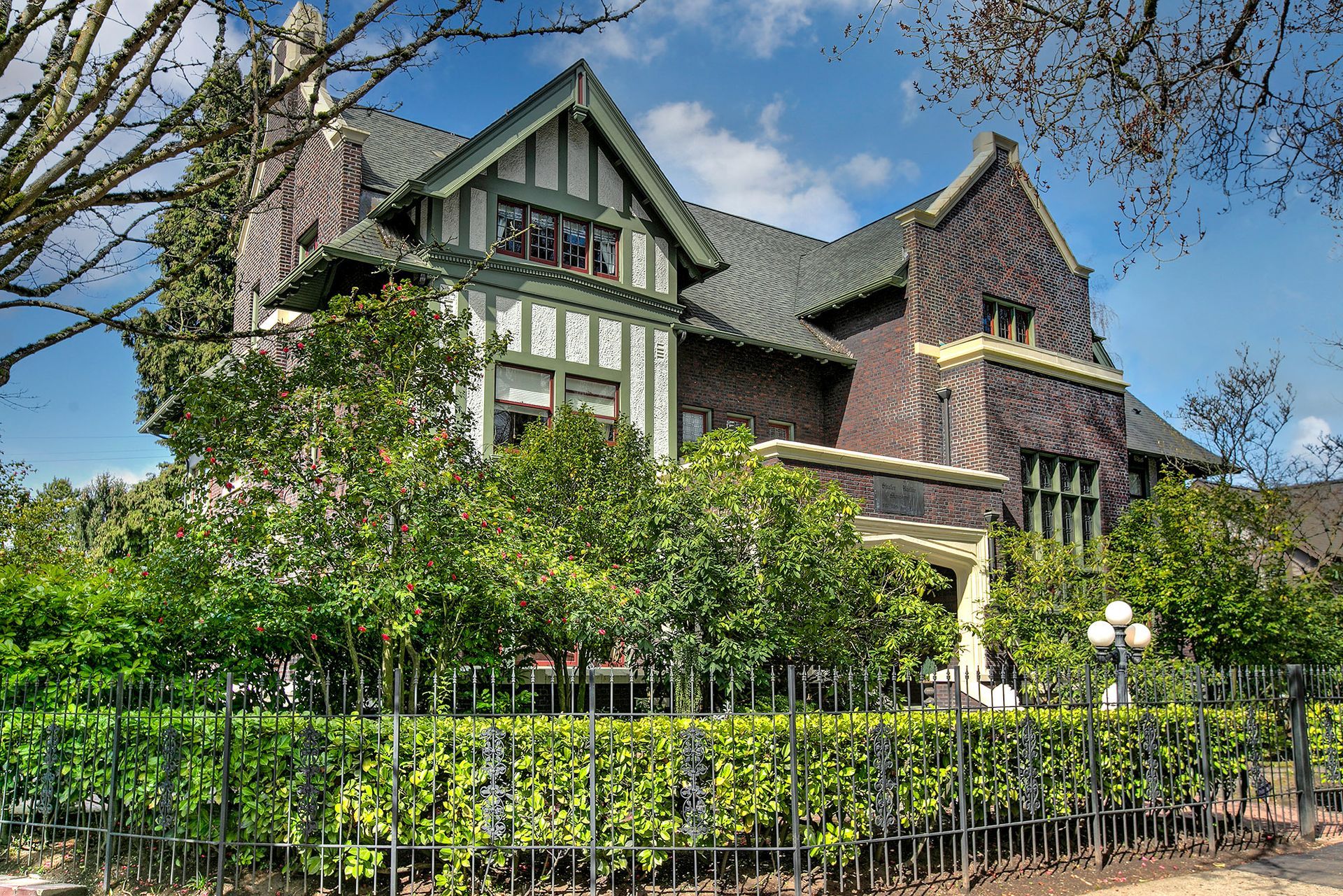 A large brick house with a fence around it and trees in front of it.