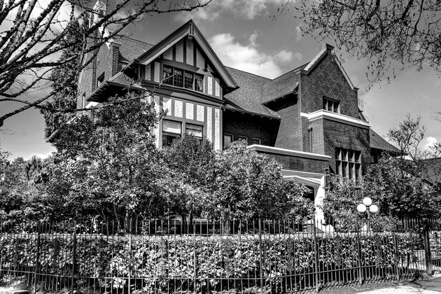 A black and white photo of a large brick house surrounded by trees and bushes.