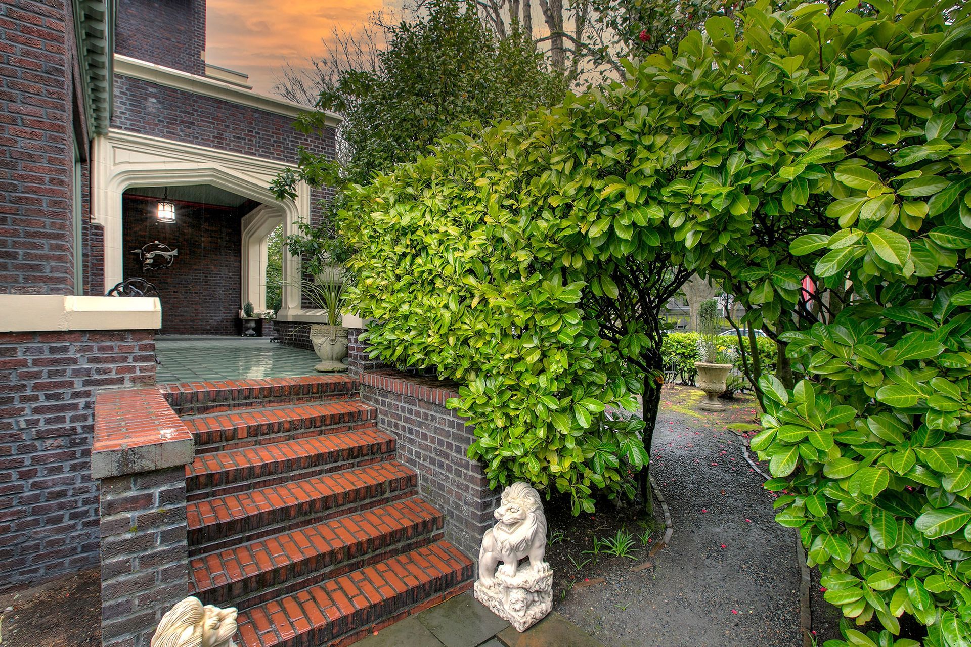 A brick house with stairs leading up to the front door surrounded by trees and bushes.