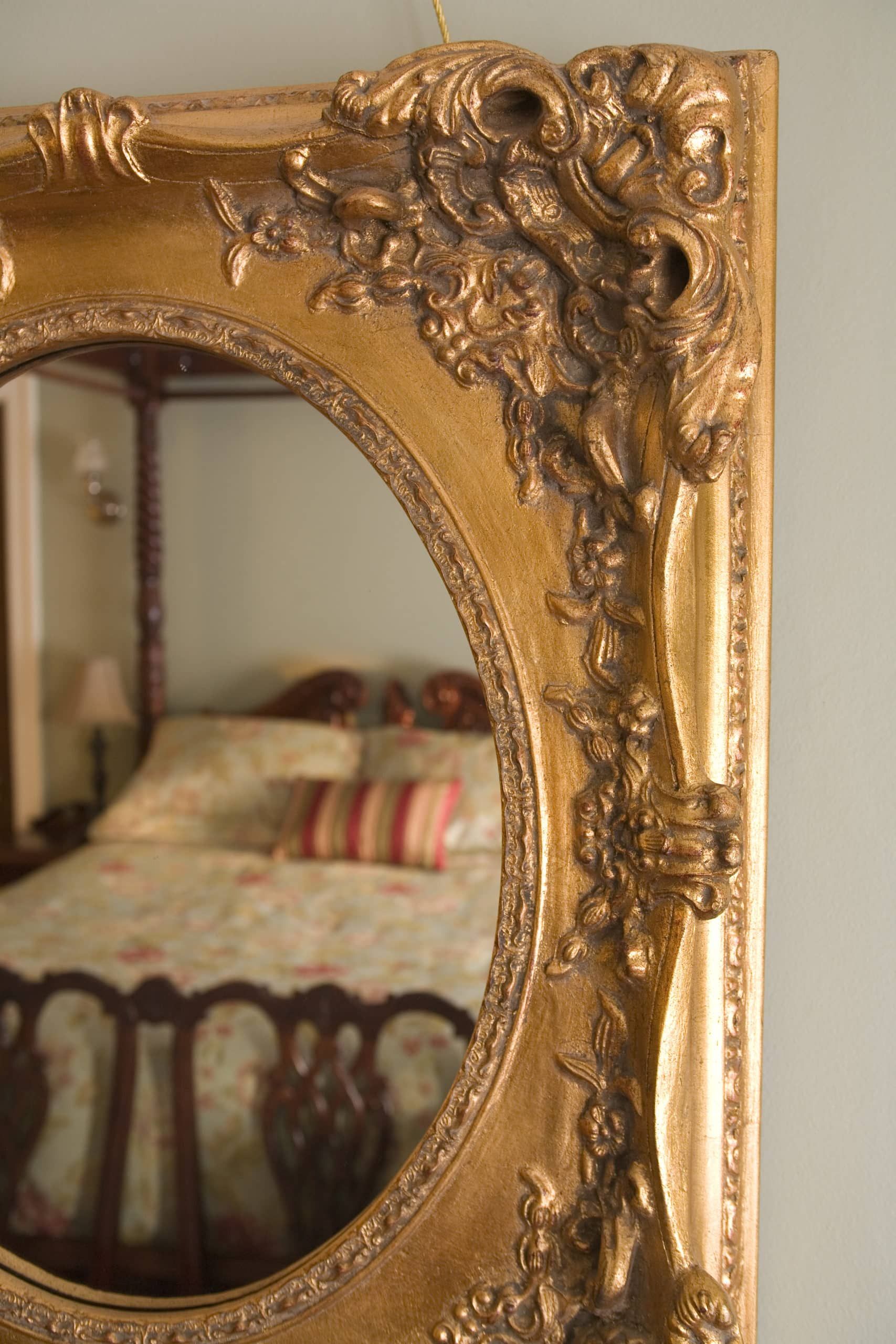A bed is reflected in a mirror with a gold frame