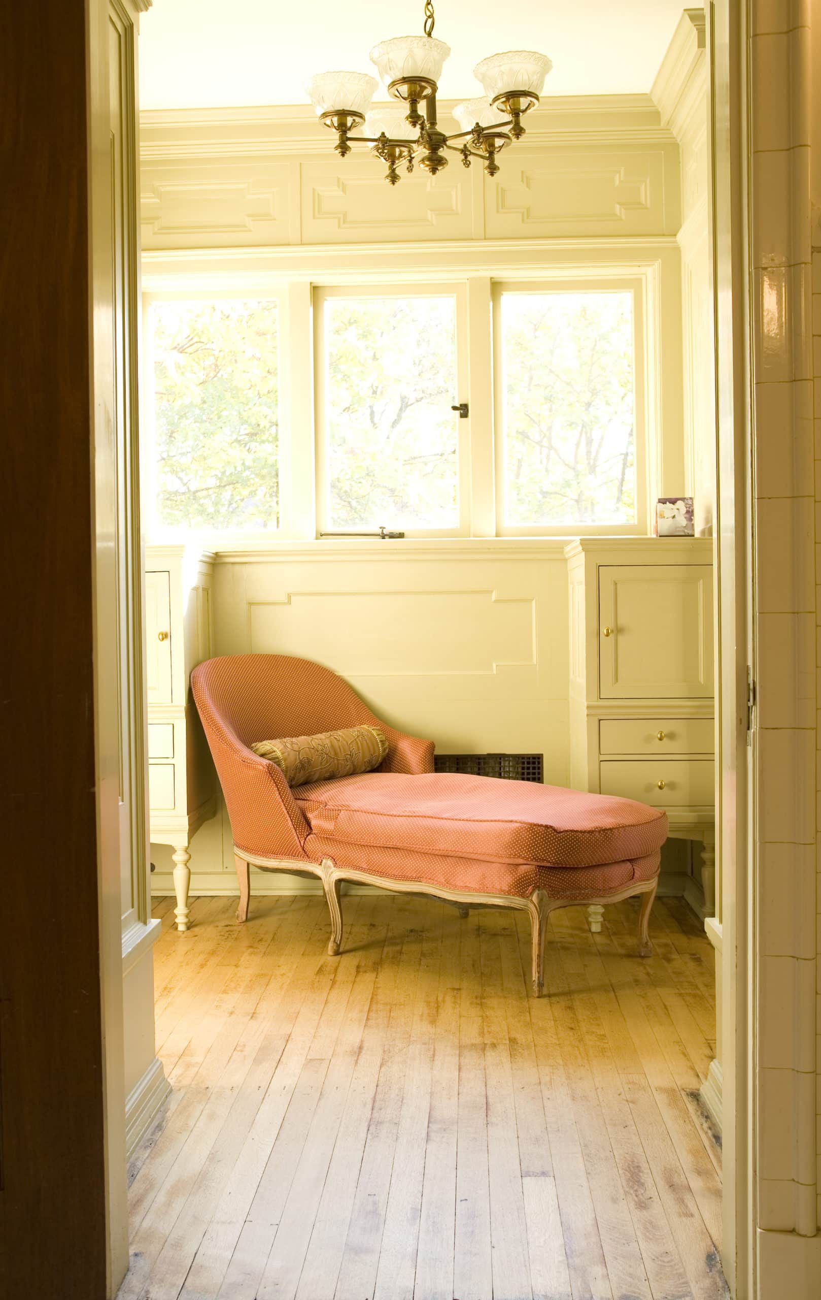 A pink chaise lounge is sitting in a room next to a window.