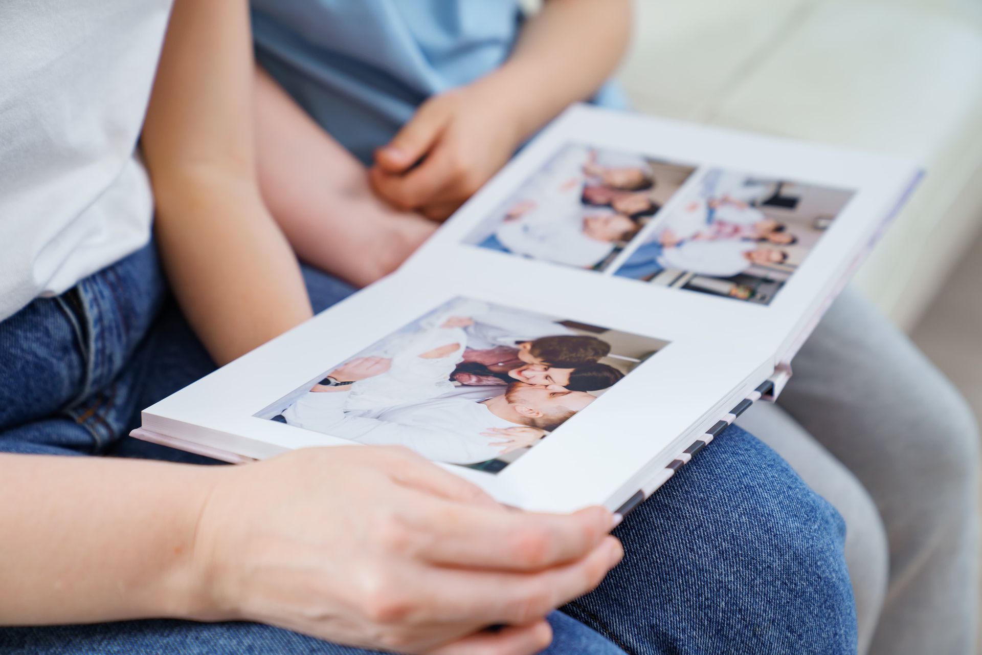 A person sits holding an open photo album, showing pictures of groups of people, with another person sitting beside them.