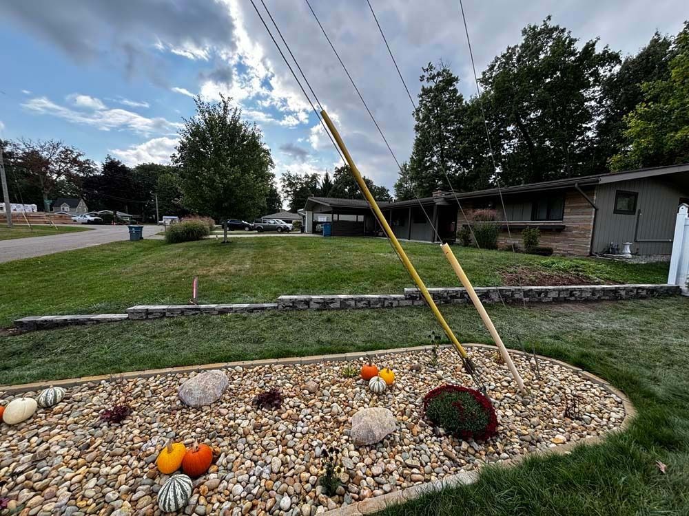 A landscaped rock garden with colorful pumpkins in front of a house, featuring two tall yellow poles leaning together.