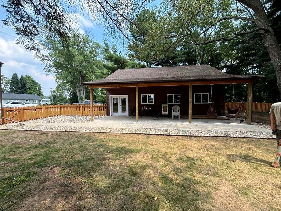 A brown cabin with a large covered patio featuring stone flooring and white French doors, surrounded by a wooden fence.