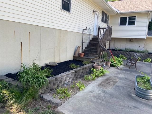 A beige house with light-colored siding, a concrete foundation, and wooden stairs leading to an elevated entry.