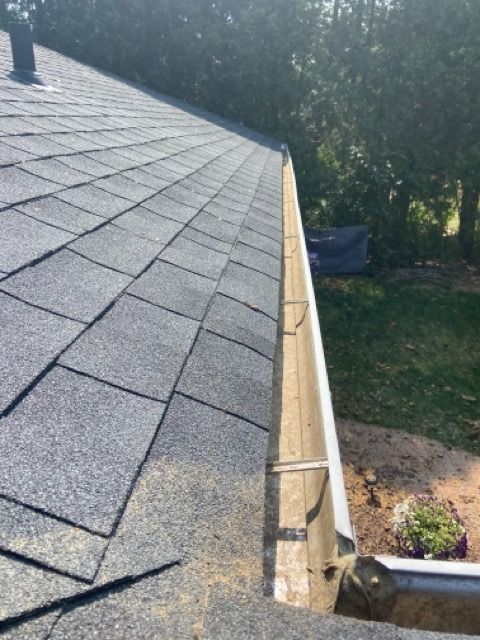 A view looking down along a gray shingled roofline next to an empty, light-colored rain gutter outdoors.