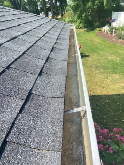 A view from above looking along a residential roof edge, showing gray asphalt shingles and a metal rain gutter.