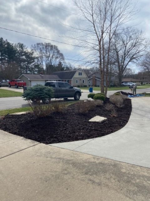 A residential front yard features a freshly mulched curved landscape bed with shrubs alongside a concrete driveway.