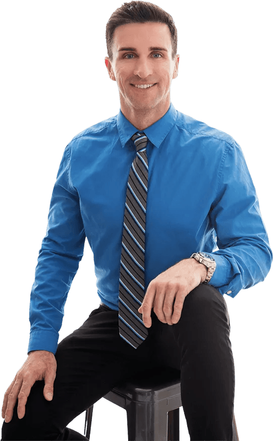 A man in a blue shirt and tie is sitting on a stool.