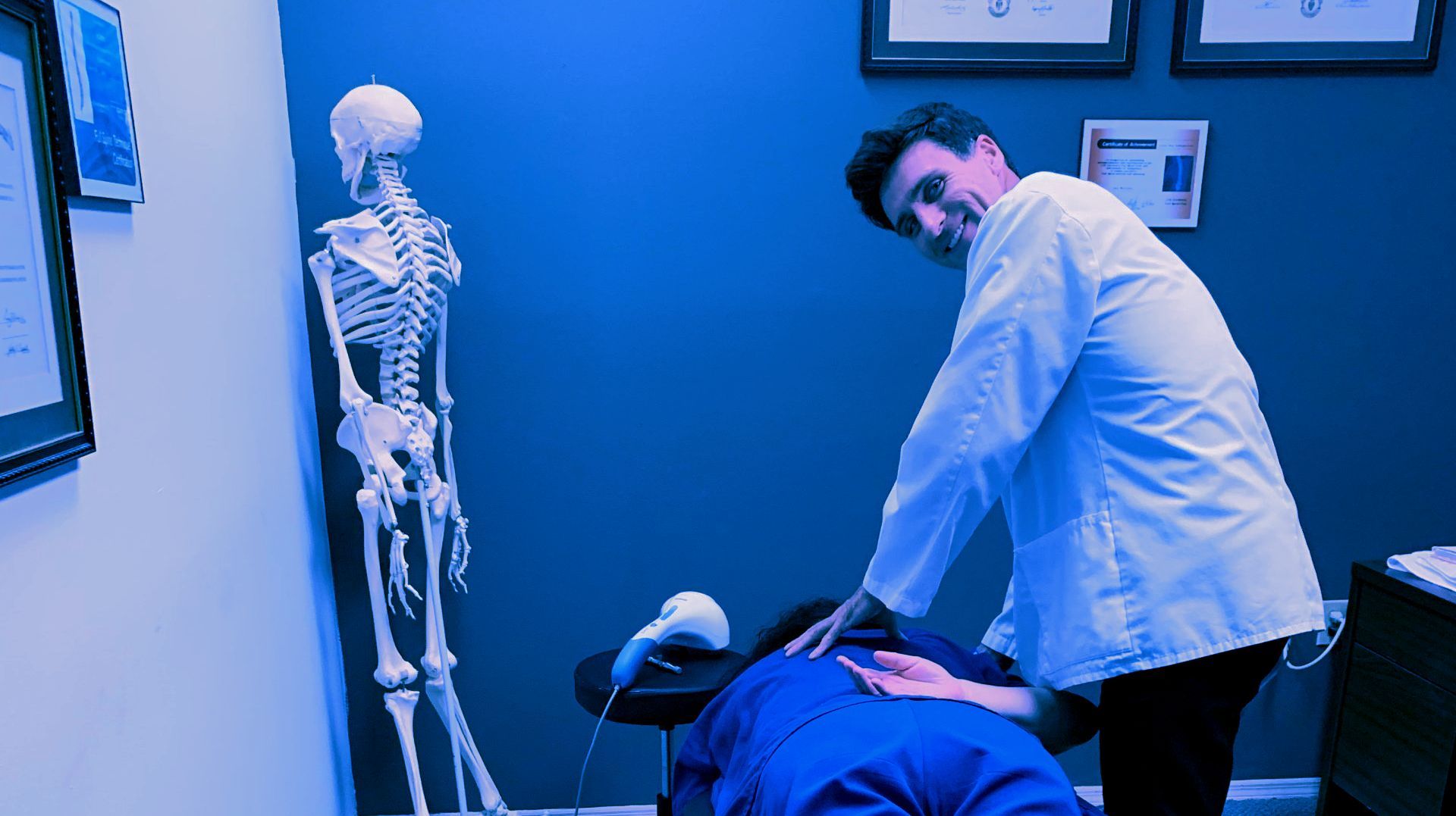 A doctor is giving a patient a massage in a blue room with a skeleton in the background.