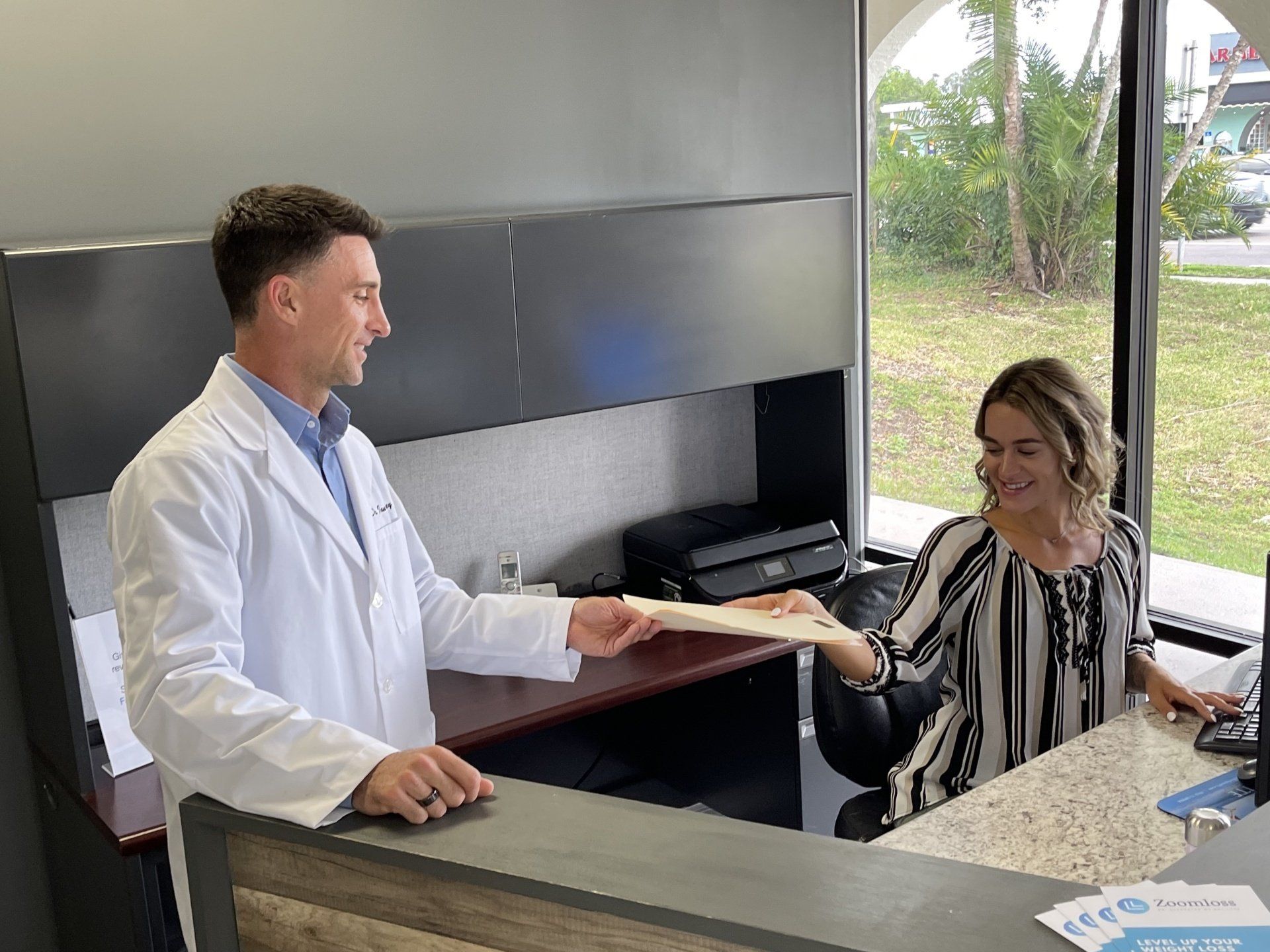 A man in a lab coat is giving a woman a piece of paper.