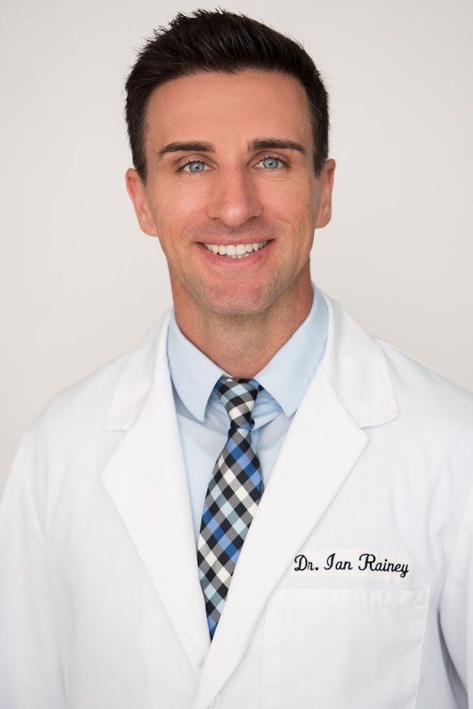 A man in a lab coat and tie is smiling for the camera.
