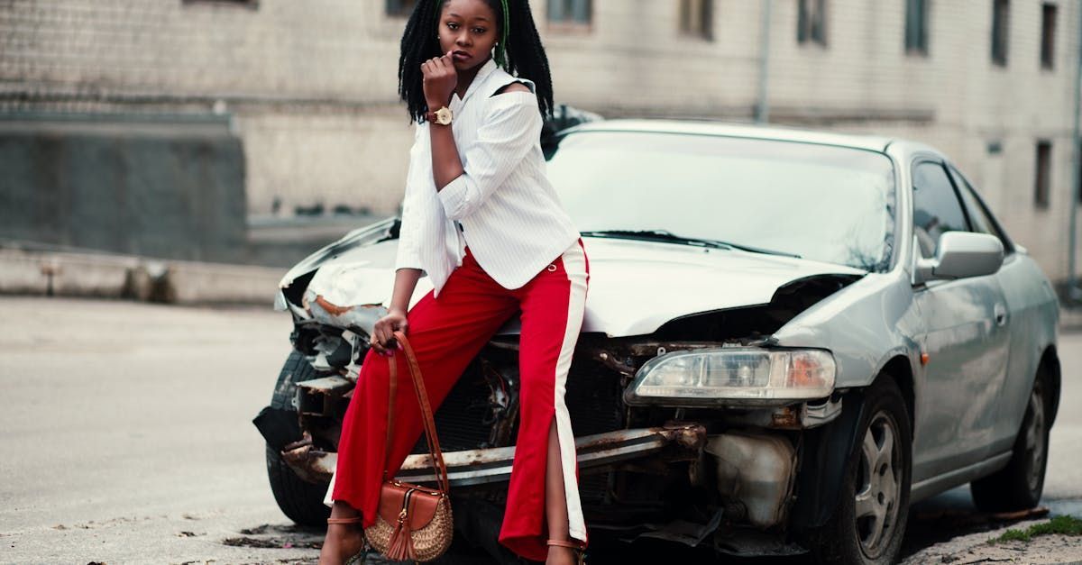 A woman in red pants is standing next to a damaged car.