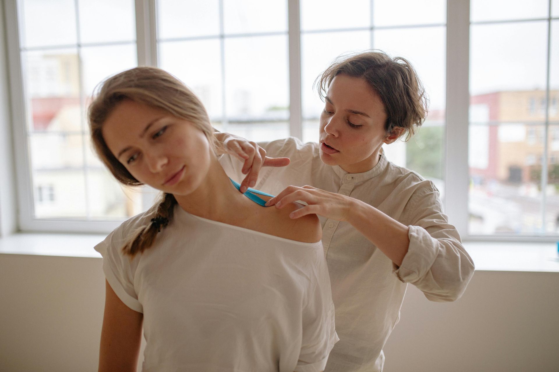 A chiropractor applying kinesiology tape to a patient's shoulder.