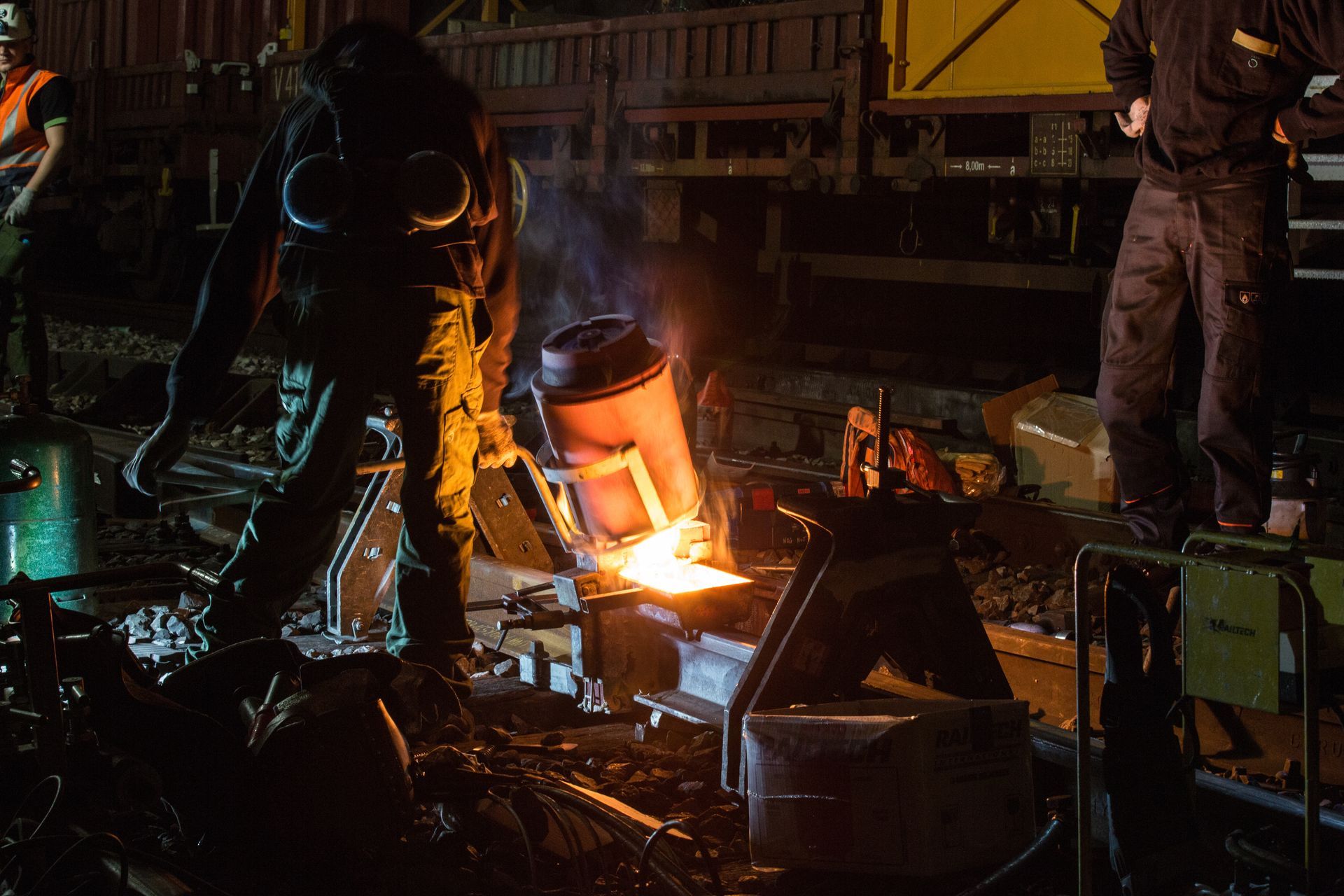 Worker pouring molten metal in a dim industrial foundry, with bright orange sparks and machinery nearby