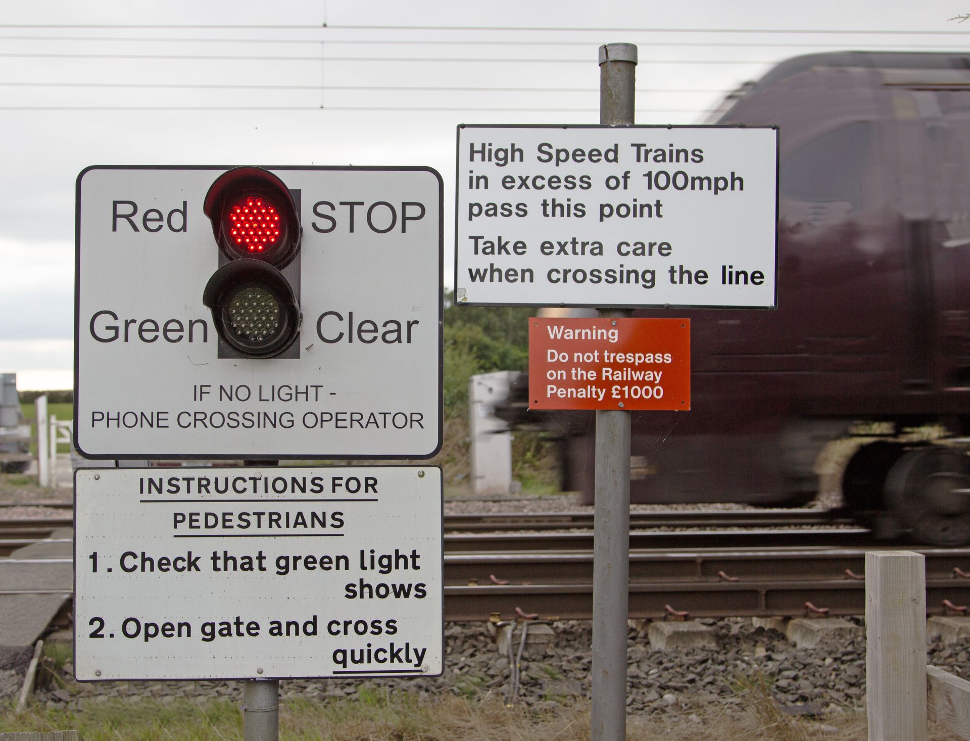 Railroad crossing with red stop light, green clear signal, and safety instruction signs by tracks