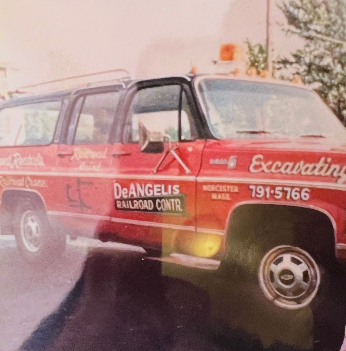 Red DeAngelis Railroad Contractors pickup truck with “Excavating” signage, parked on a wet street