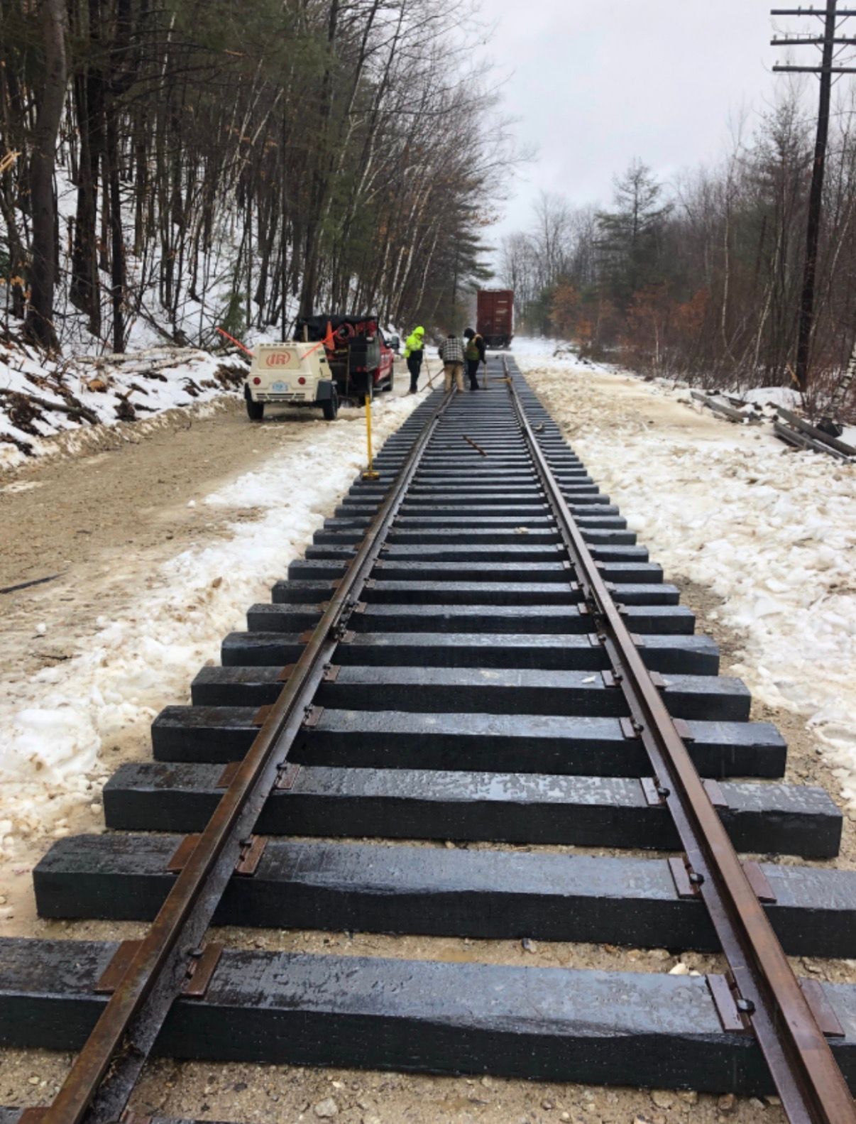 Workers repairing railroad track in a snowy wooded area
