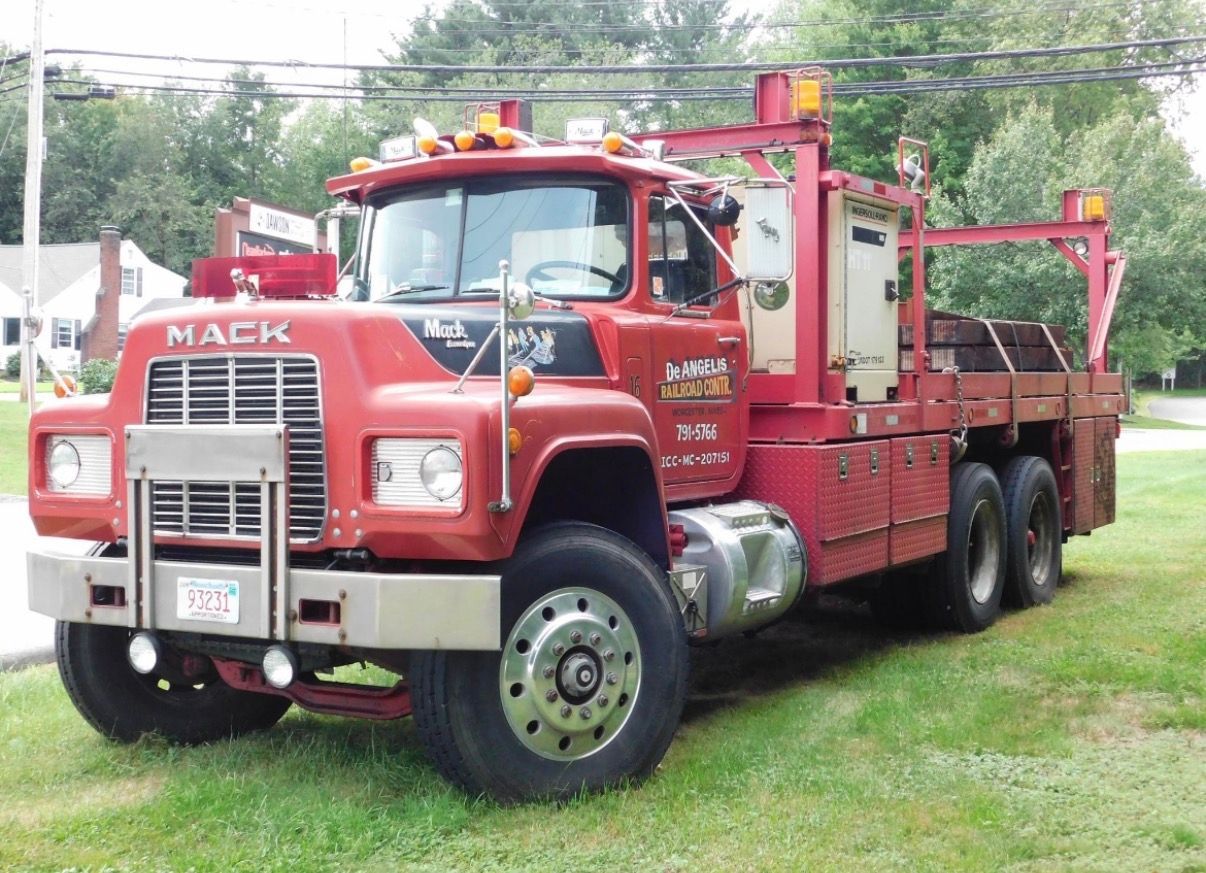 Red Mack tow truck parked on grass, with red body and chrome grille.