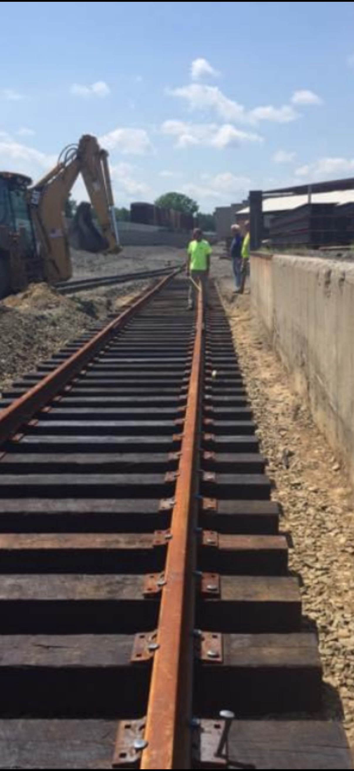 Railway track under construction with workers and excavator on a sunny day.