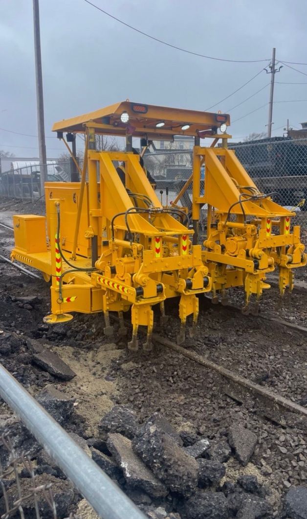 Worker in a yellow vest inspecting railroad tracks on a gravel rail bed