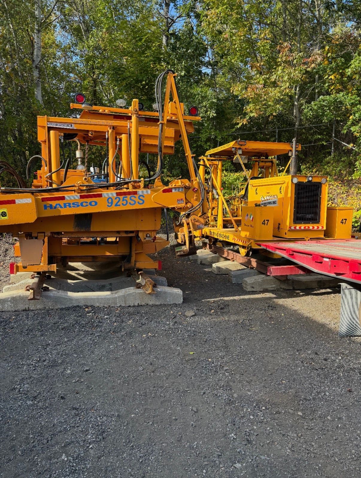 Yellow construction machinery on gravel, with trees in the background and a red platform beside it