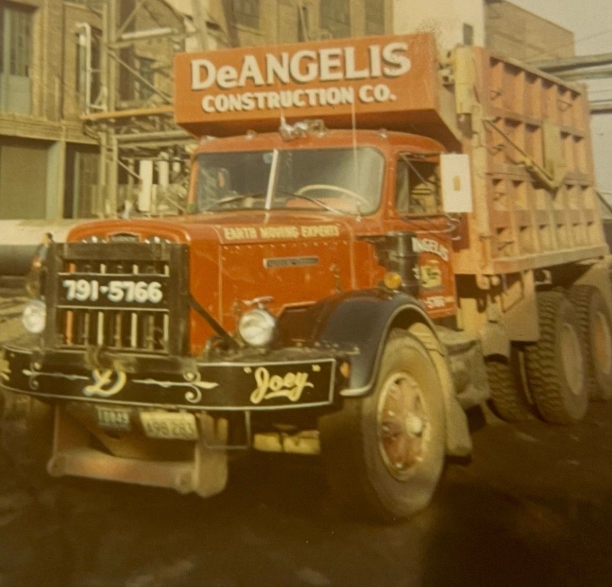Vintage orange DeAngelis Construction Co. dump truck on a dirt road, front view
