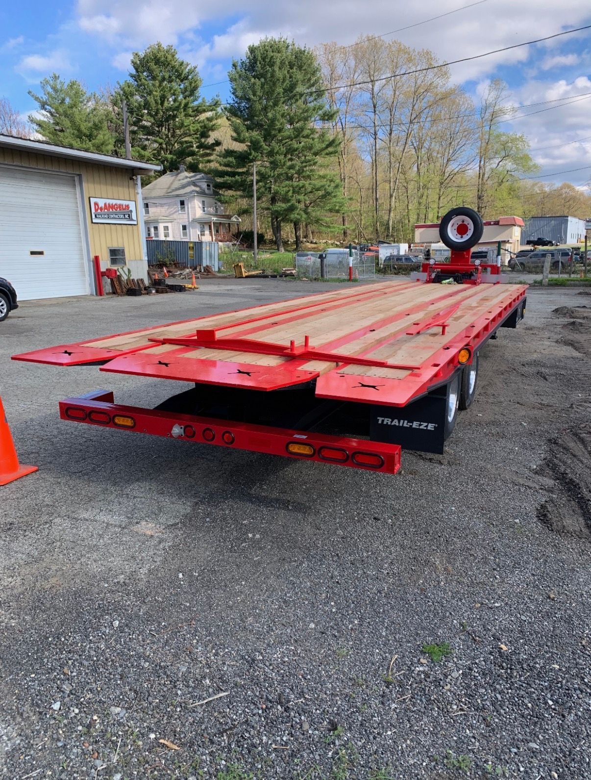 Red flatbed trailer on gravel lot, viewed from the rear with a target-like marker at the front.