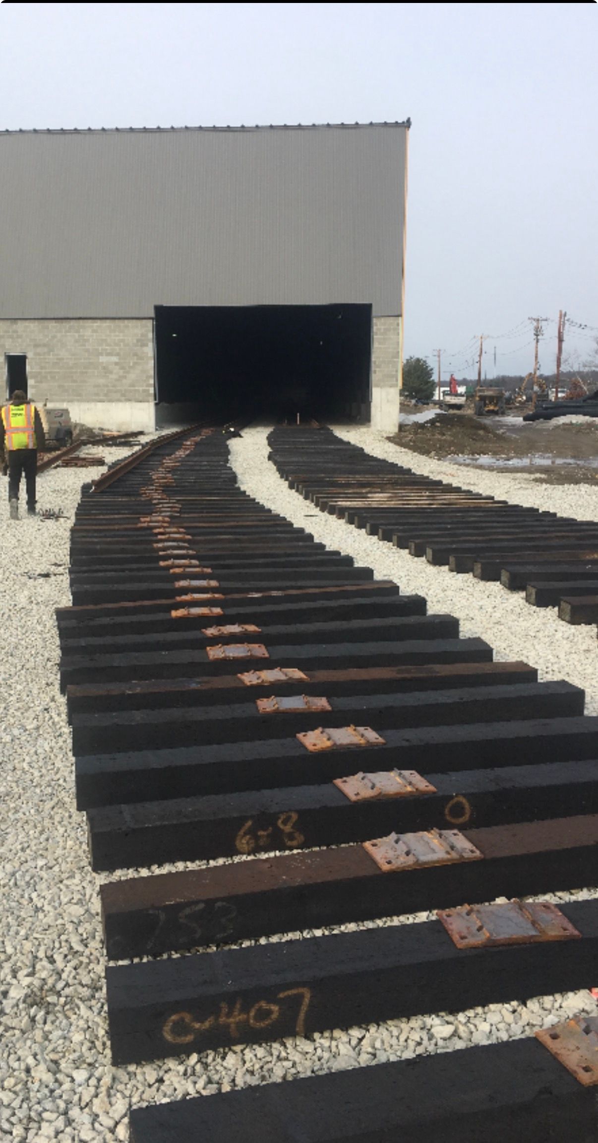 Railroad track section leading into a large industrial building, with a worker in a yellow vest nearby.