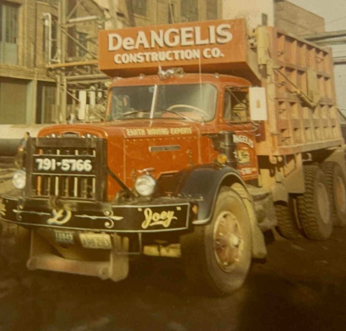 Vintage orange DeAngelis Construction Co. dump truck on a work site, front view with load bed and license plate 791-5766