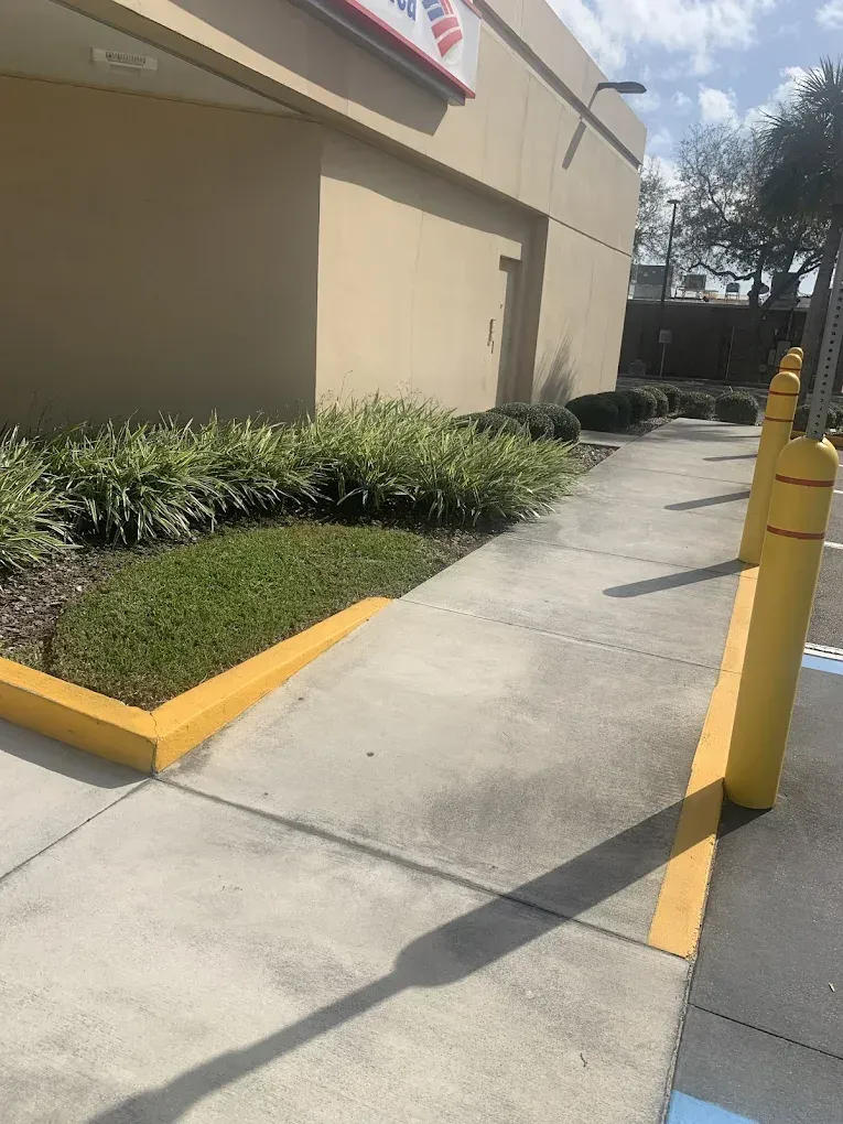 A sidewalk with a yellow curb and a yellow pole in front of a building.