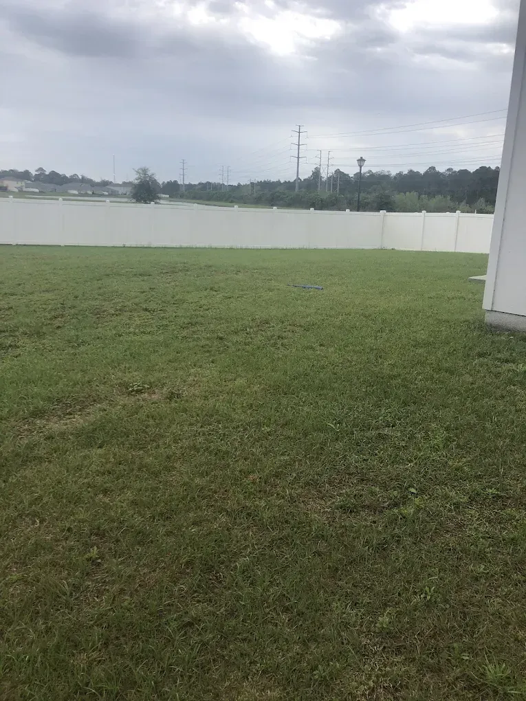 A large lush green lawn with a white fence in the background.