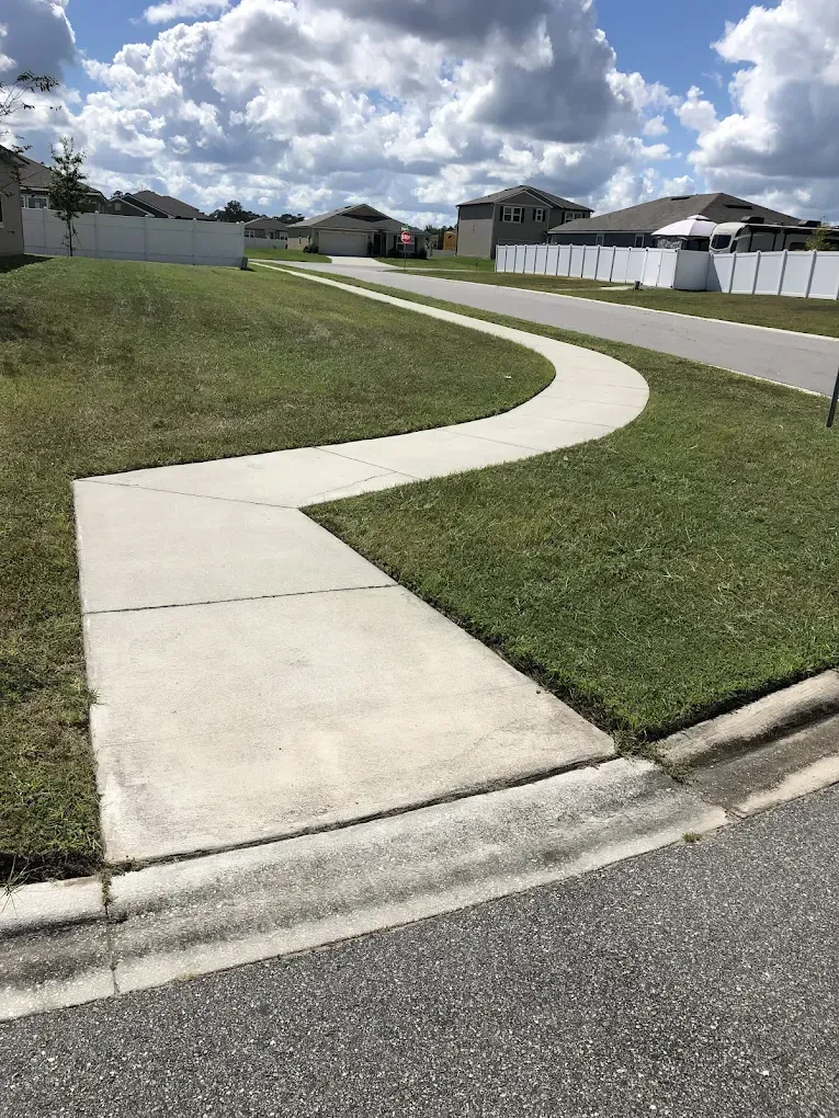 A concrete sidewalk leading to a grassy yard in a residential neighborhood.