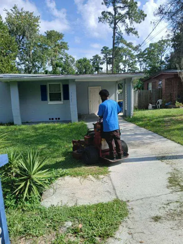 A man is using a lawn mower to cut the grass in front of a house.