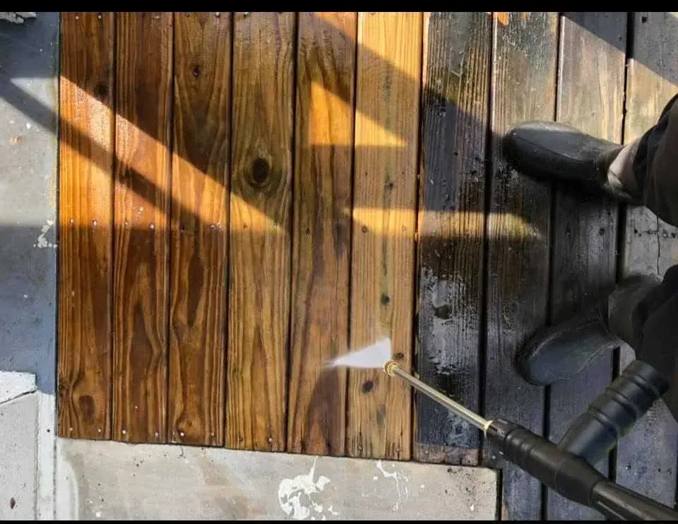 A person is cleaning a wooden deck with a high pressure washer.