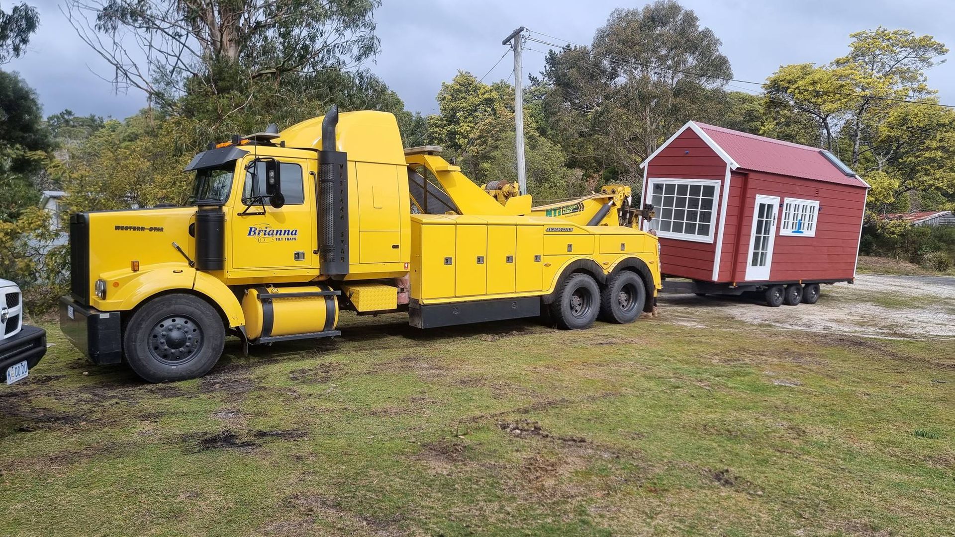 A yellow tow truck is towing a small red house.